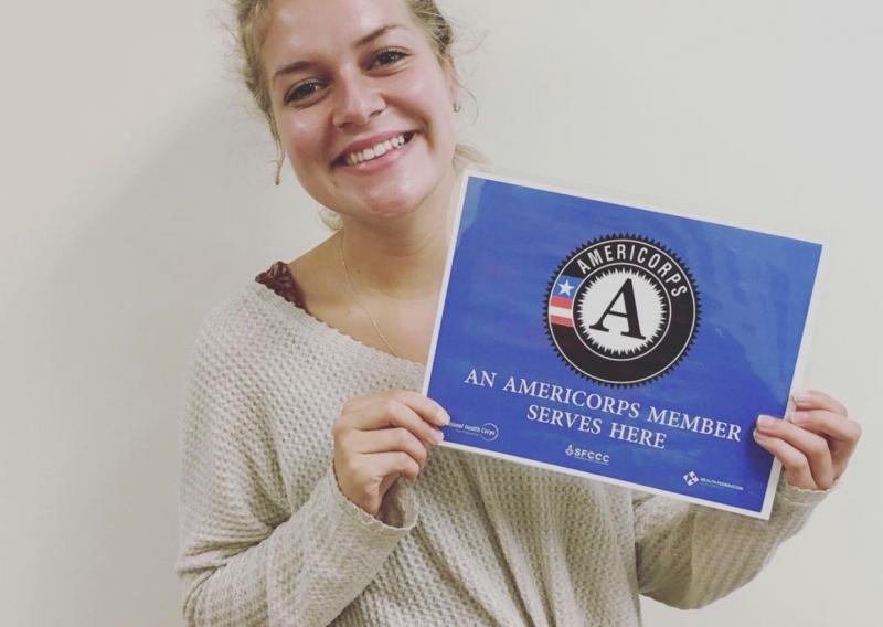 Lauren Hall holding an "AmeriCorps member serves here" sign at Curry Senior Center.