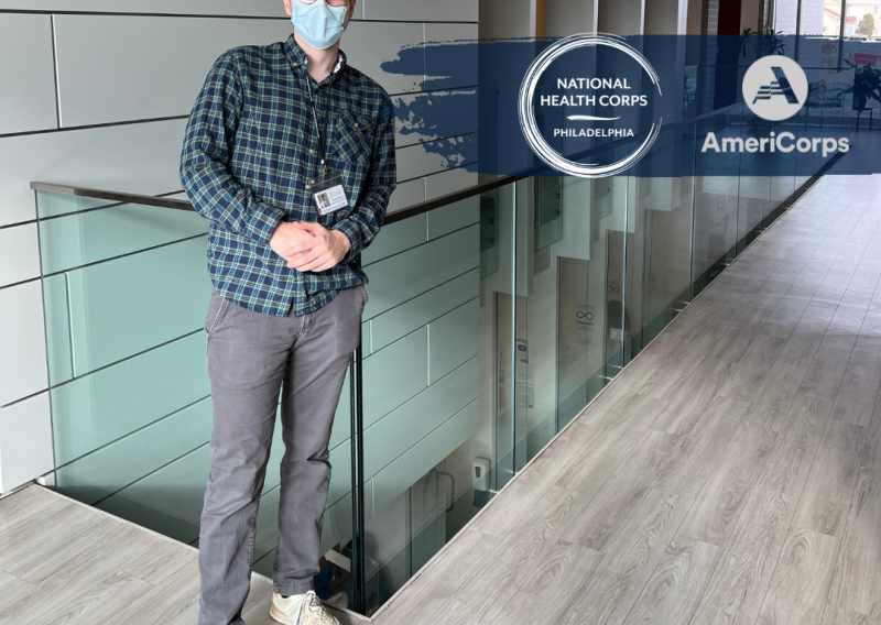 Corey standing near a banister with the NHC and AmeriCorps logos added in next to him