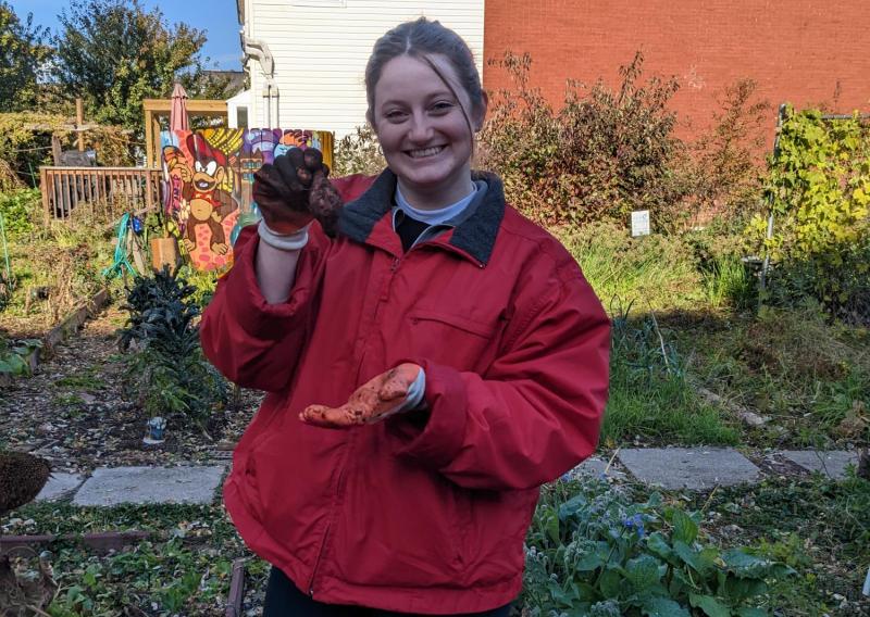 Shannon is standing in a garden holding a vegetable.