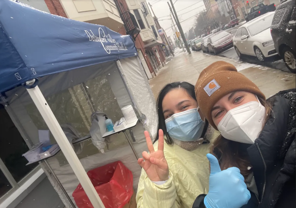 A selfie of Anne and another person wearing masks on a snowy day in front of a covid testing tent