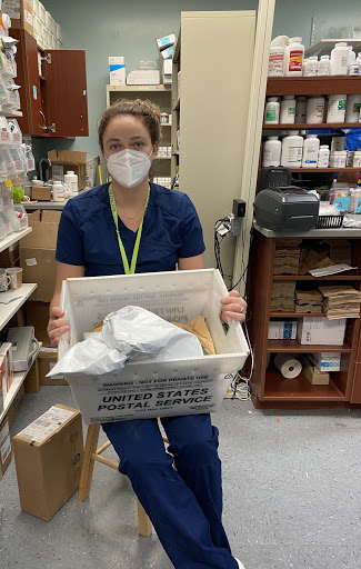 A person in navy blue scrubs holding a box of medications