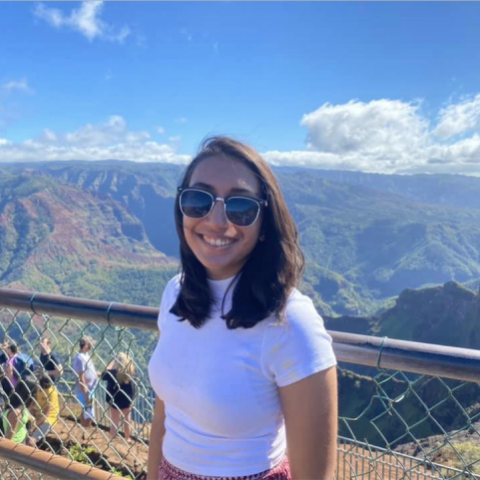 NHC PGH member Chinmayi smiling on a sunny day with a scenic mountainous background wearing sunglasses