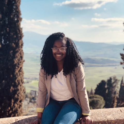 NHC PGH member Gabby sitting on a stone wall with a scenic outdoor background