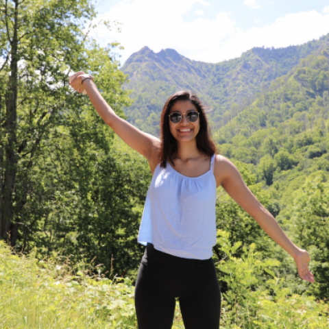 NHC PGH member Geeta smiling and holding her arms diagonal with sunglasses on and a mountain in the background