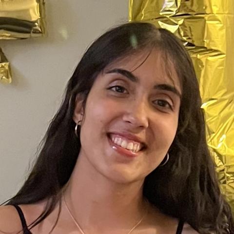 Anjalie Gowda is in the center of the frame, facing the camera and smiling.