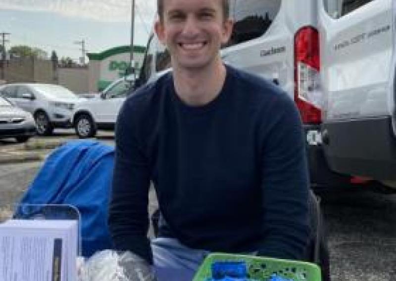 NHC PGH member Brett smiling at a health event outside, behind a table of health education materials