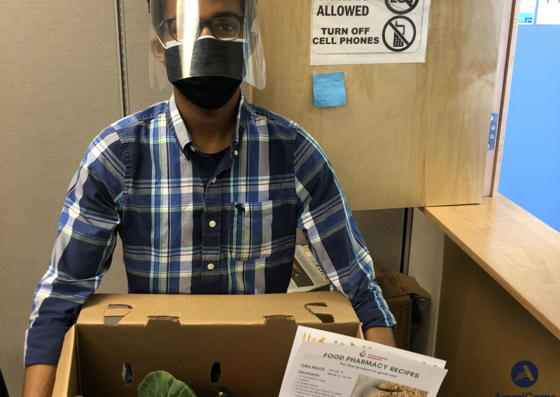 NHC SF Member Spencer Robinson holding a box of produce and a recipe for patients at Food Pharmacy.