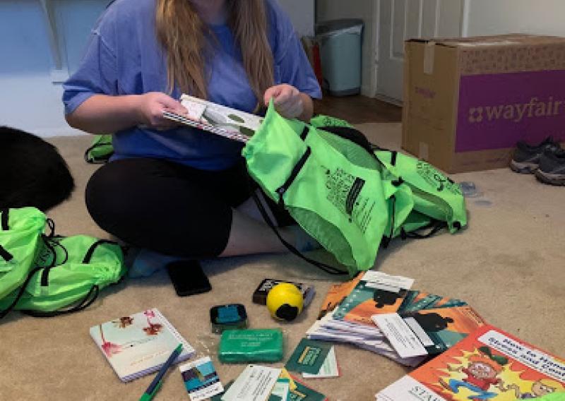 NHC member Paige sitting on the floor filling green bags with items called wellness kits