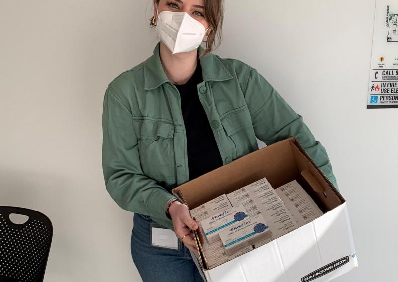 Vjola Jorgji is facing the camera directly. She is wearing a facmask. She is holding a box with Rapid COVID-19 tests to be distributed to patients.