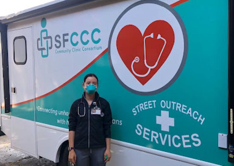 A person stands in front of a mural that reads "SFCCC" in the upper left-hand corner and "Street Outreach Services" in the lower right corner.