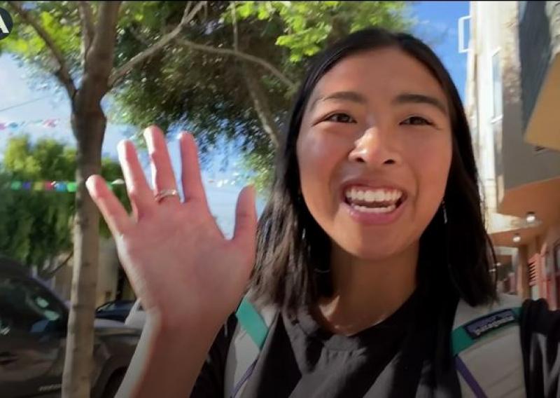 A person is facing the camera and smiling while waving at the audience.