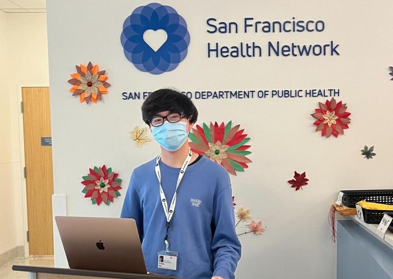 A person stands behind the podium facing the camera. Behind the person is a wall with the San Francisco Health Network logo.