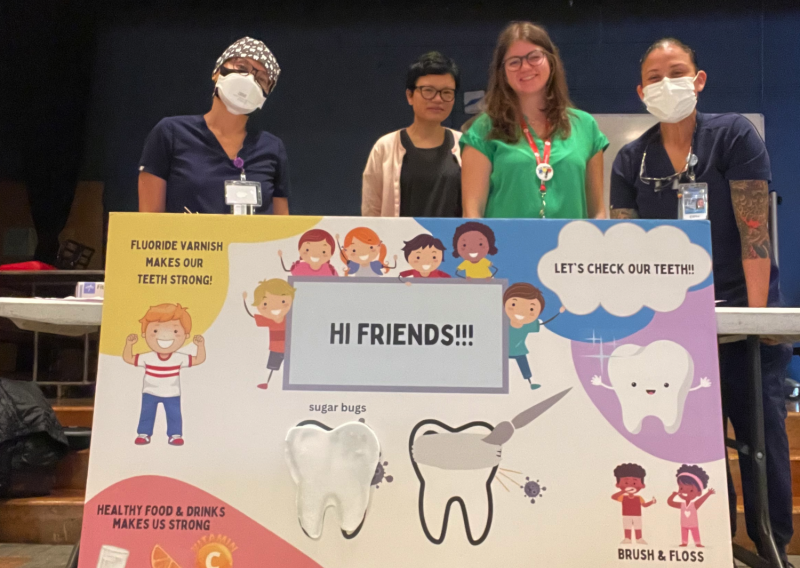 Emily standing with her colleagues behind a poster advocating for practices that help maintain healthy teeth for children. 