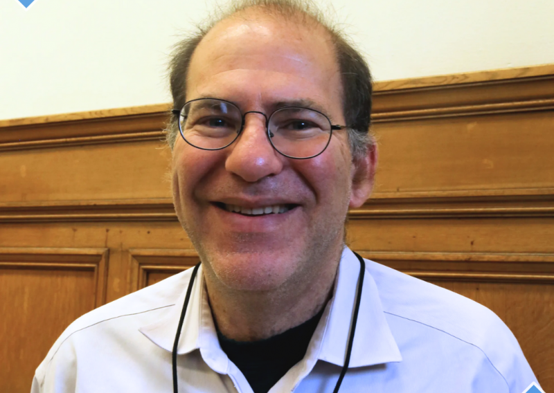 Dr. Barry Zevin is standing in the middle of the frame, facing the camera and smiling.