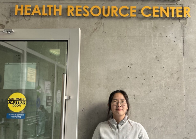 Tammy is facing the camera and smiling. She is standing under a sign that reads "Maria x Martinez Health Resource Center". 
