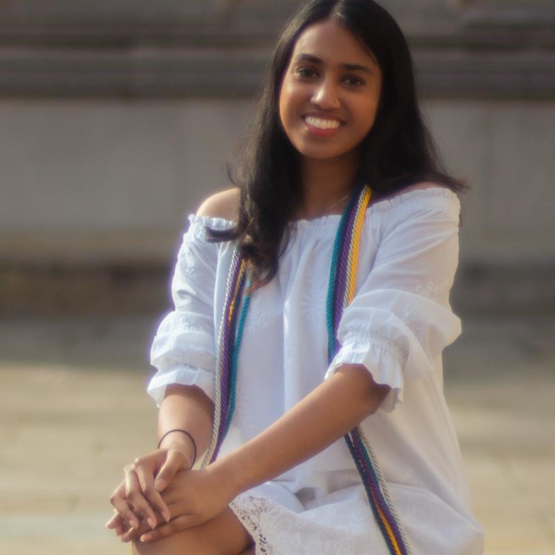 Anisha is sitting outside in front of a building.