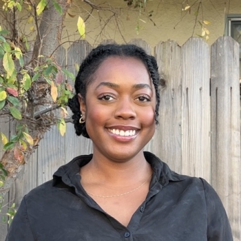 Tia Halsey stands in the middle of the frame, facing the camera and smiling.