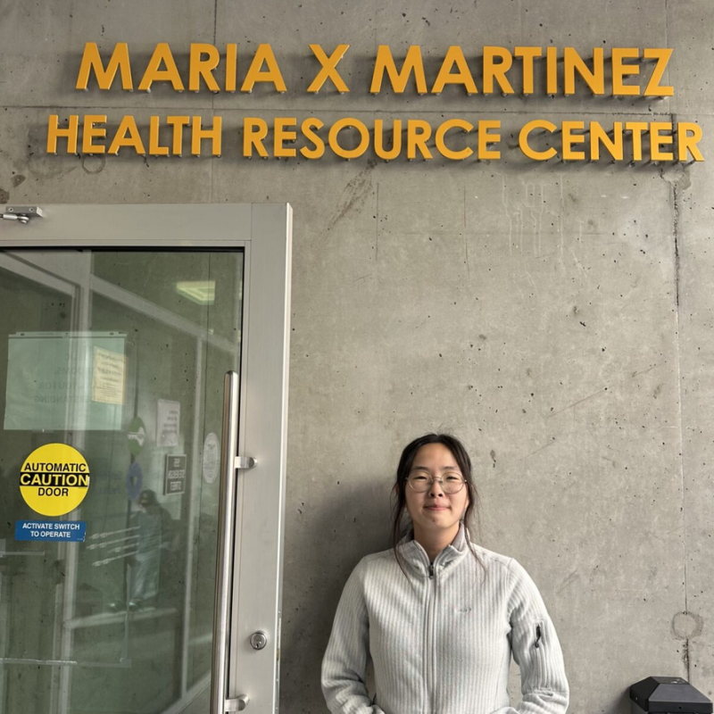 Tammy is facing the camera and smiling. She is standing under a sign that reads "Maria x Martinez Health Resource Center". 
