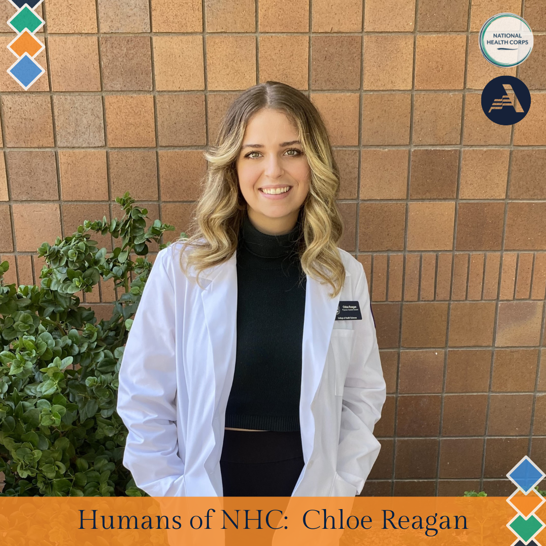 Chloe Reagan stands in the middle of the frame, facing the camera and smiling. Chloe is wearing a white coat over a black turtleneck.