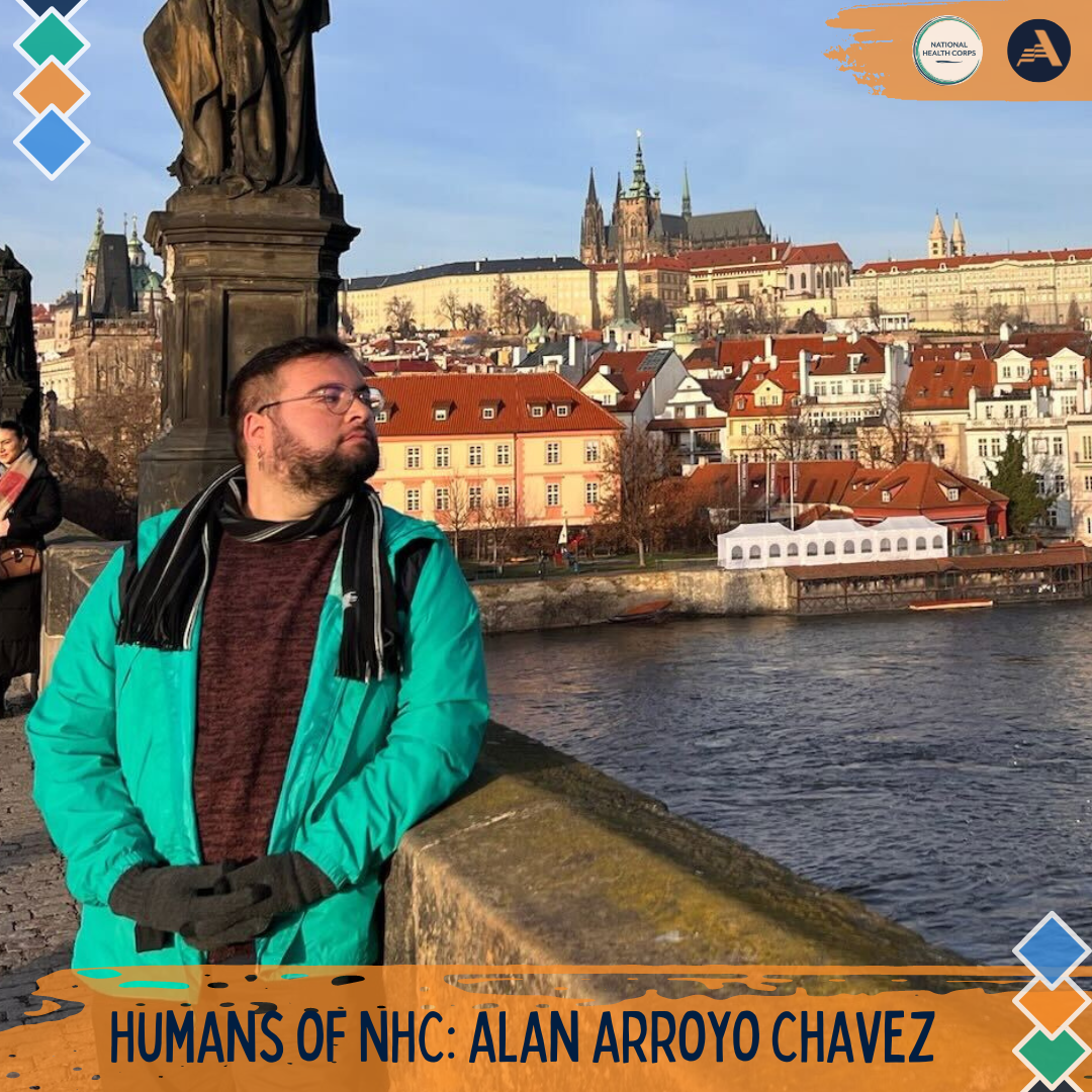 Alan is standing to the left of the camera frame, looking to their left. They are standing on a bridge, and behind them is the Prague skyline. 