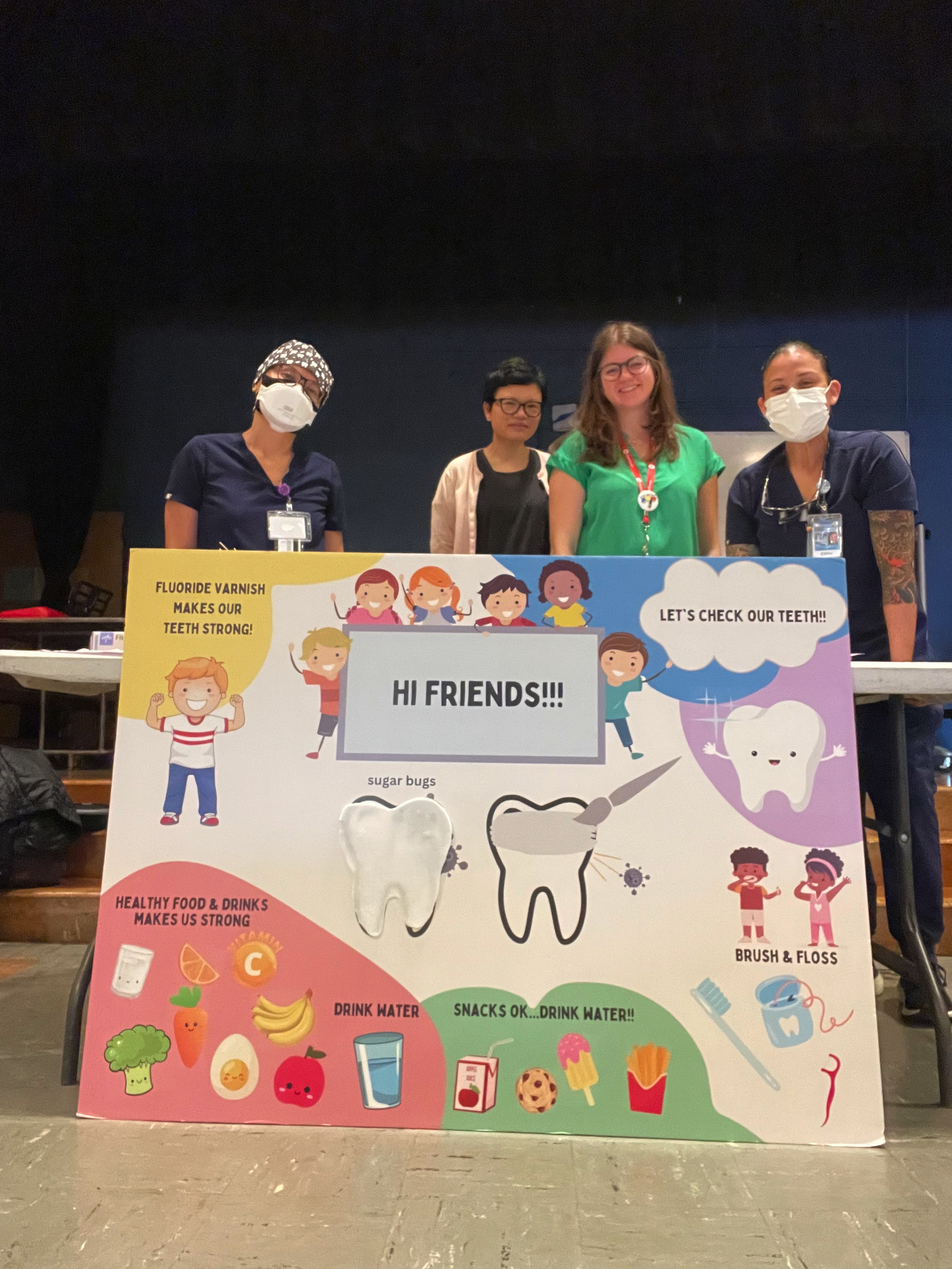 Emily standing with her colleagues behind a poster advocating for practices that help maintain healthy teeth for children. 