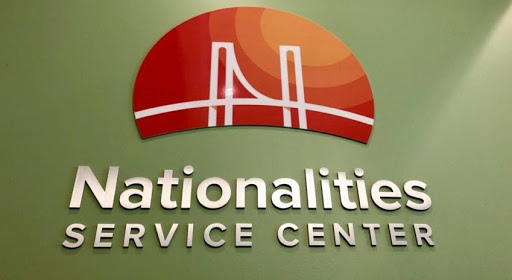 a green wall with an orang half circle logo with a bridge silhouette, under the logo reads Nationalities Service Center 